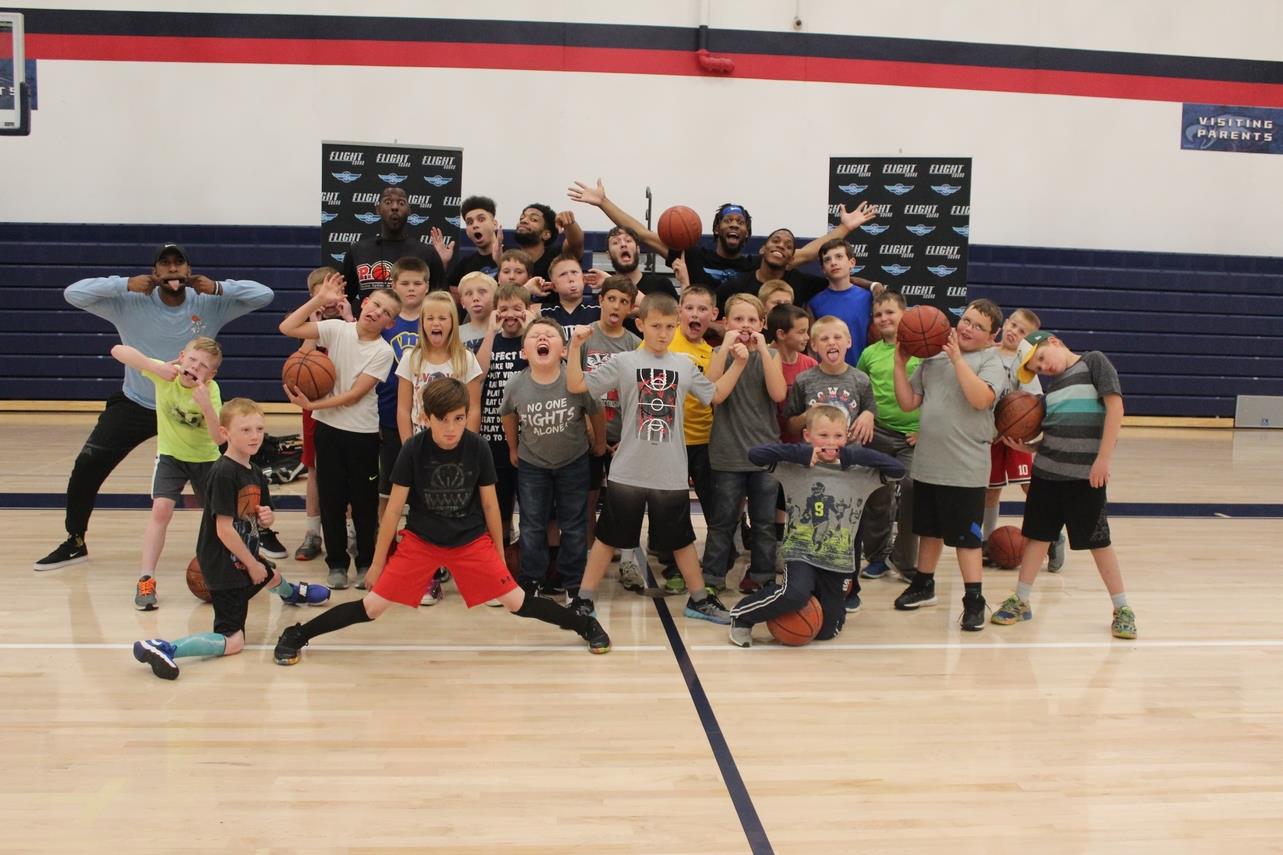 Group of adults and kids inside a gym posing with basketballs